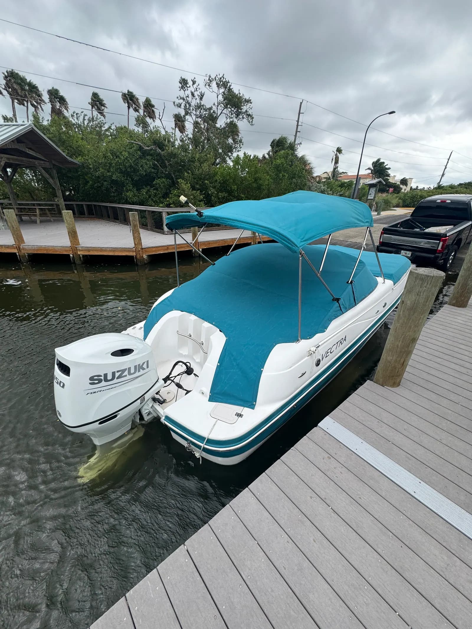 Vectra deck boat with a new teal bimini top and matching mooring cover, Suzuki outboard, at a canal dock