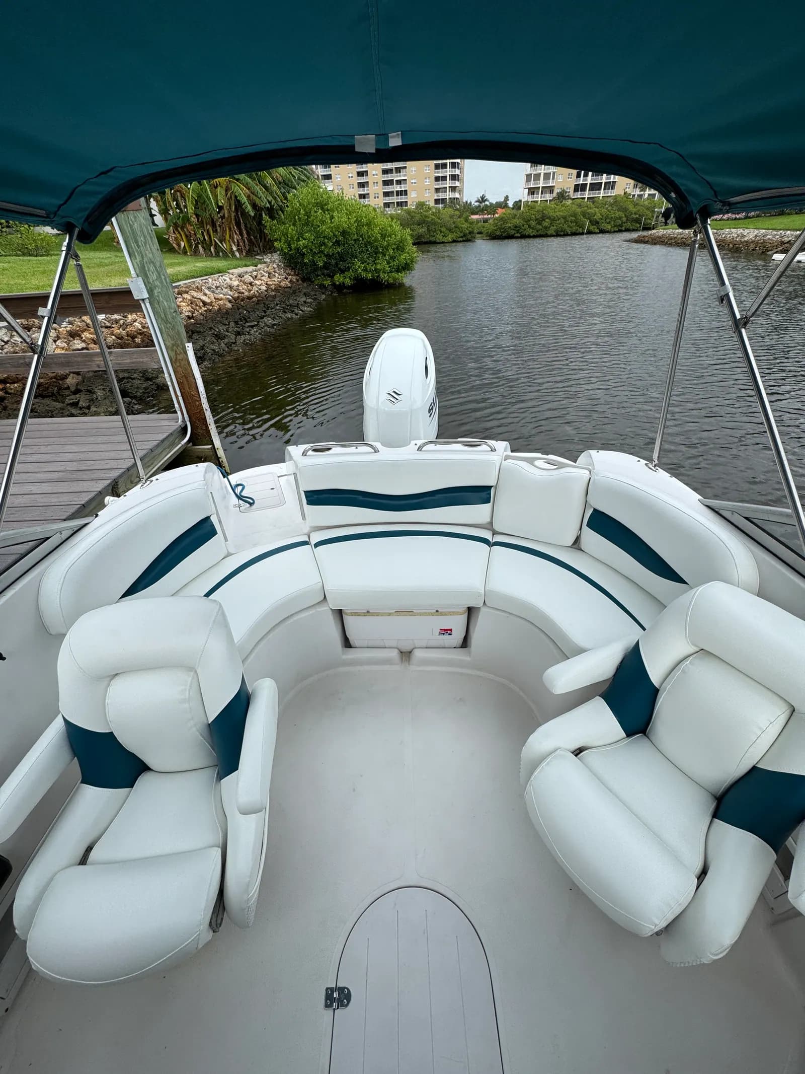 White marine vinyl wraparound seating with teal accent panels under the bimini on a deck boat